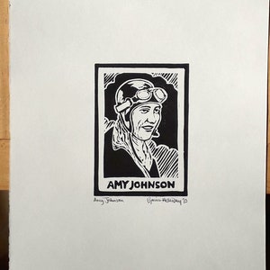 Peut inclure: Gravure sur linoléum en noir et blanc d'une femme portant un casque et des lunettes. L'estampe est intitulée "AMY JOHNSON" et signée par l'artiste "Yvonne Holloway '23".