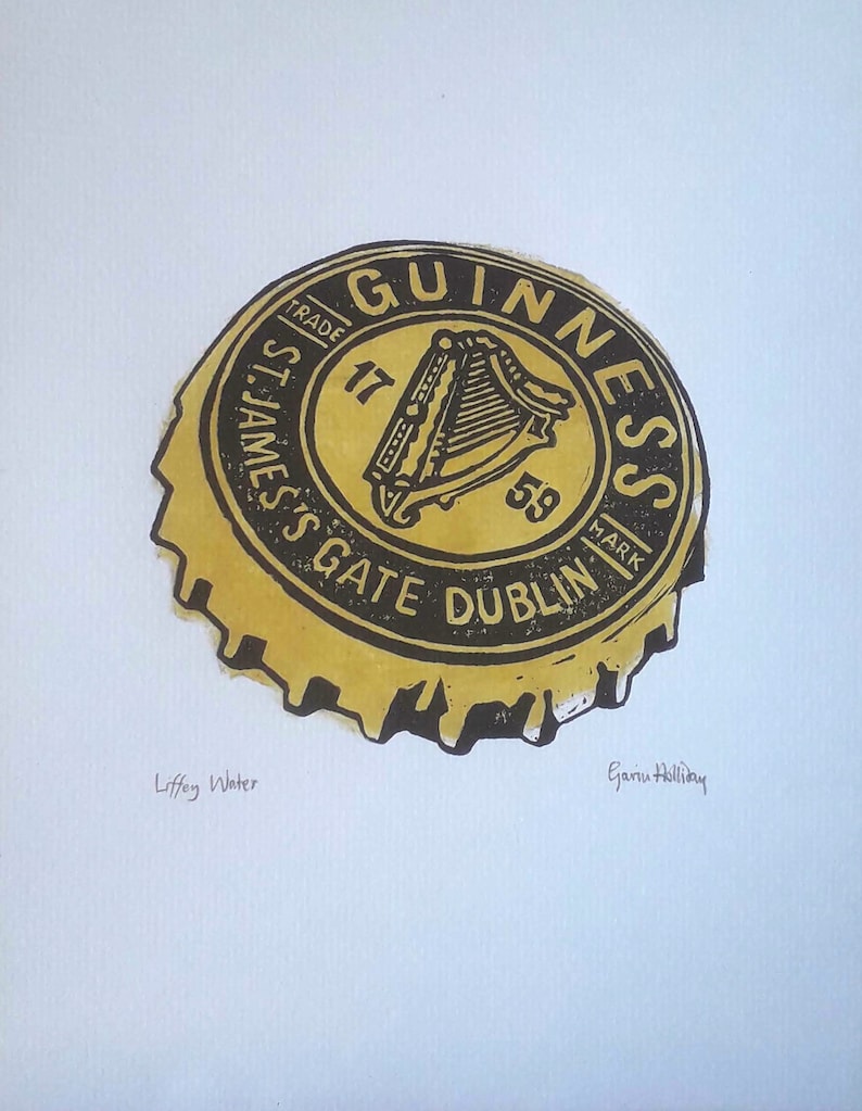 Op de afbeelding: Een afdruk van een Guinness-flesdop. De dop is geel en zwart, met het Guinness-logo en tekst. De tekst "St. James's Gate Dublin" is zichtbaar. De afdruk bevat ook de tekst "Liffey Water" en de handtekening van de kunstenaar.