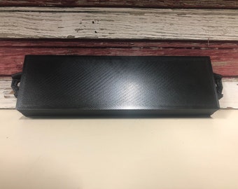 May include: A black rectangular box with a textured surface and two small handles on either side.