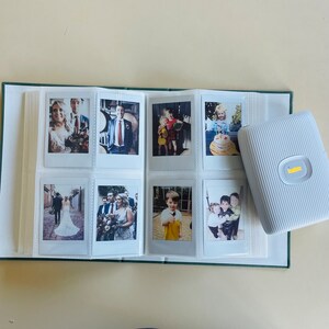 May include: A white photo album with green trim and a white portable photo printer. The album is open to reveal photos of a wedding, children, and a family.
