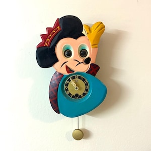 May include: Vintage Mickey Mouse wall clock. The clock features a colorful design with Mickey Mouse in a festive outfit. The clock face is teal, with a gold pendulum. The clock is made of wood and is a collectible item.