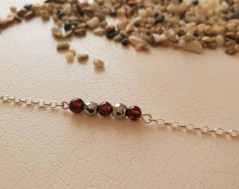 May include: A silver chain bracelet with five beads, including three dark red beads and two silver beads.