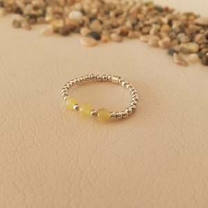 May include: A silver ring with three yellow beads. The ring is on a light brown surface.
