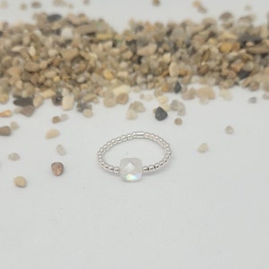 Peut inclure: Une bague en argent avec une pierre précieuse blanche au centre. La bague est faite de petites perles d'argent.