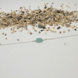 May include: A delicate silver chain bracelet with a single square-shaped light green gemstone.