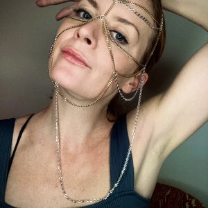 May include: A woman wearing a gold and silver chain headpiece that covers her eyes and forehead. The chain is connected to a long silver chain necklace.