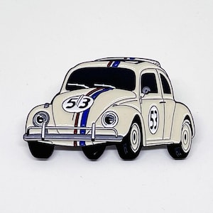 Op de afbeelding: Crèmekleurige emaille pin van een klassieke auto, met een zwart dak en wielen. De auto heeft blauwe en rode racestrepen en het nummer "53" op de deuren en motorkap. Een verzamelobject in vintage stijl.