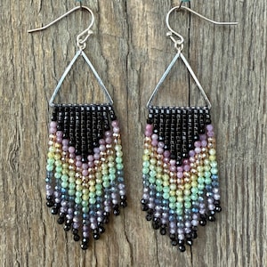 May include: Handmade beaded earrings with a geometric design. The top section is black, transitioning into a rainbow of colors including pink, yellow, green, and blue. The earrings hang from silver-colored hooks.