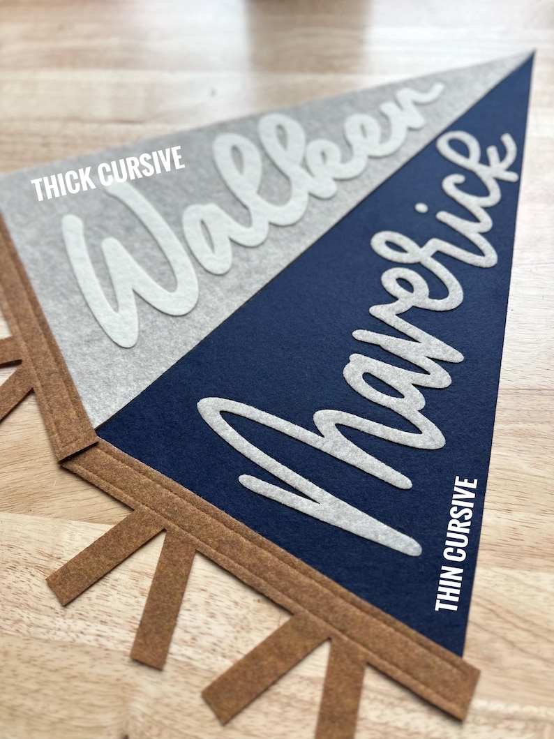 May include: A triangular felt pennant featuring a split design of light gray and dark navy blue. The word Walker is written in white thick cursive, and the word Maverick is written in white thin cursive. The pennant has brown felt tabs.