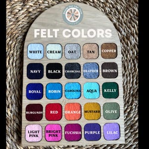 May include: An arched wooden display board titled FELT COLORS featuring twenty-five square felt swatches in various shades including white, cream, oat, tan, copper, navy, black, charcoal, heather, brown, royal, robin, carolina, aqua, kelly, burgundy, red, orange, mustard, olive, light pink, bright pink, fuchsia, purple, and lilac.