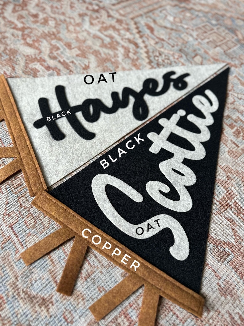 May include: Two triangular felt pennants with copper-colored tabs at the base. The top pennant is oat-colored with the black text "Hayes" in script. The bottom pennant is black with the white text "Scottie" in script. Labels indicate color options.