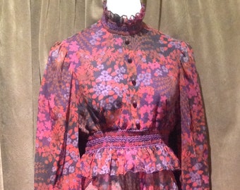 May include: A long-sleeved dress with a floral print in shades of pink, purple, and black. The dress has a high neck and a ruffled hem.
