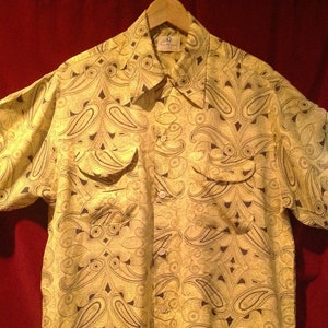 May include: A yellow short-sleeved shirt with a paisley pattern in black. The shirt has a button-down collar and two pockets.