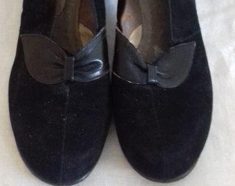 May include: A pair of black suede heeled shoes with a black leather bow detail on the front.