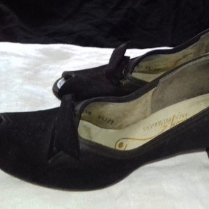 May include: A pair of black peep-toe heels with a low heel. The shoes are made of a soft, suede-like material and have a simple, elegant design.