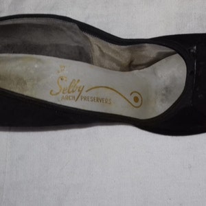 May include: Black suede shoe with a bow on the toe. The insole is white with the text "Selby Arch Preservers" in gold.