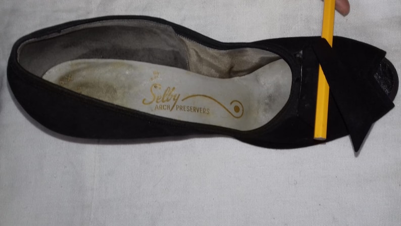 May include: Black suede shoe with a bow on the toe. The insole is white with the text "Selby Arch Preservers" in gold.