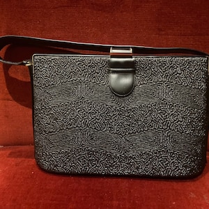 Peut inclure: Un sac à main en cuir noir avec un motif texturé et une fermeture à fermoir argenté. Le sac a une longue bandoulière et une fermeture à rabat.