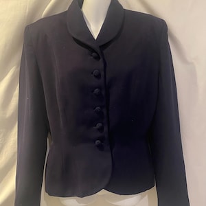 Könnte beinhalten: Ein dunkelmarineblauer Blazer mit rundem Kragen und sechs passenden Knöpfen. Der Blazer hat lange Ärmel und eine taillierte Passform, präsentiert auf einer weißen Schaufensterpuppe.