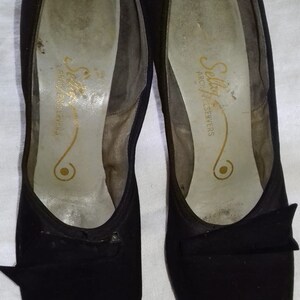 May include: A pair of black peep-toe heels with a bow detail. The shoes are made by Selkirk Arch Preservers.