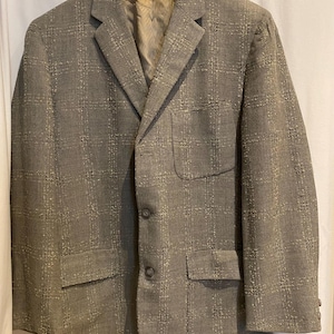 May include: A grey blazer with a textured, plaid-like pattern. The jacket has a notched lapel, two front pockets, and a chest pocket. It is buttoned with three buttons and has a light-coloured lining.