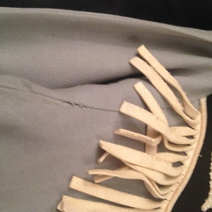May include: A light blue jacket with white fringe trim. The fringe is on the right shoulder and extends down the side of the jacket.