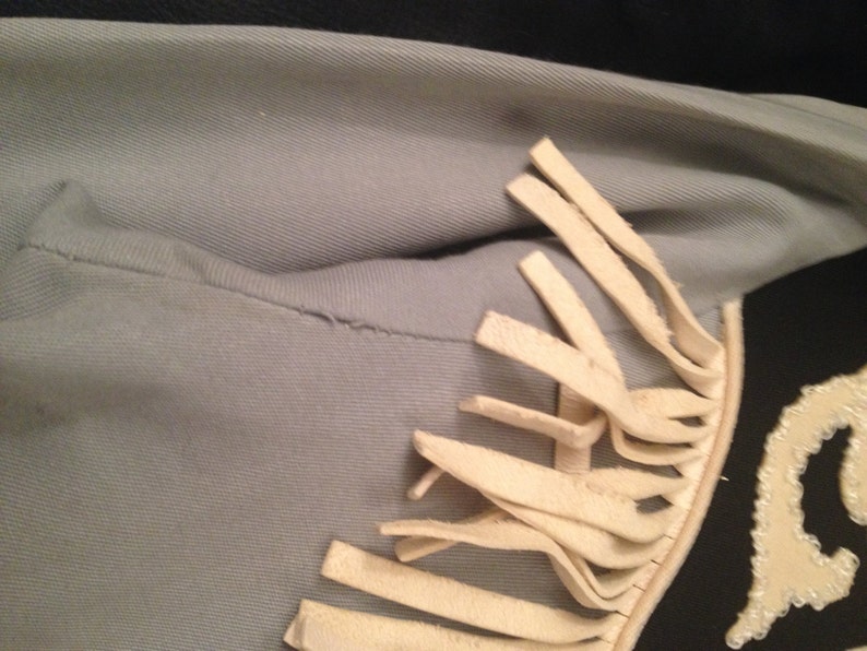 May include: A light blue jacket with white fringe trim. The fringe is on the right shoulder and extends down the side of the jacket.