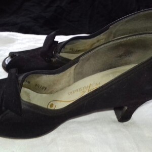 May include: A pair of black peep-toe heels with a low heel. The shoes are made of a soft, suede-like material and have a simple, elegant design.