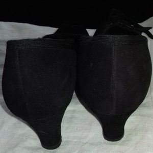 May include: A pair of black suede heeled shoes with a pointed toe. The shoes have a low heel and a simple design.