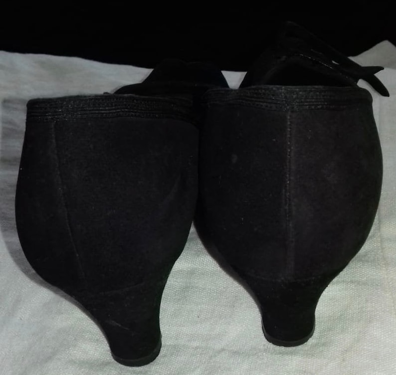 May include: A pair of black suede heeled shoes with a pointed toe. The shoes have a low heel and a simple design.
