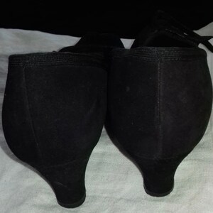 May include: A pair of black suede heeled shoes with a pointed toe. The shoes have a low heel and are in good condition.
