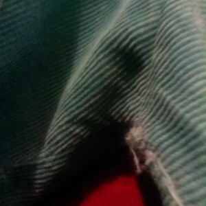 May include: A close-up of a teal corduroy fabric with a small tear in the fabric.