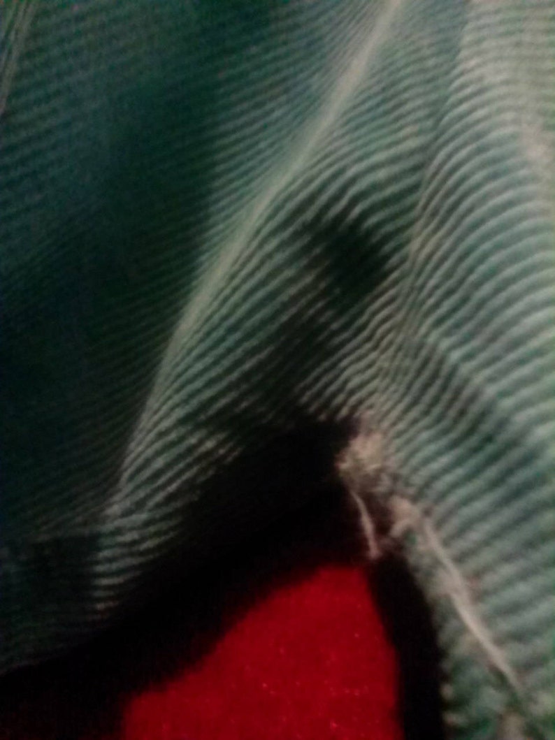 May include: A close-up of a teal corduroy fabric with a small tear in the fabric.