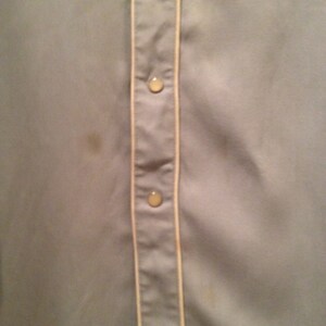 May include: A light gray button-up shirt with a white trim down the front. The shirt has three buttons visible.