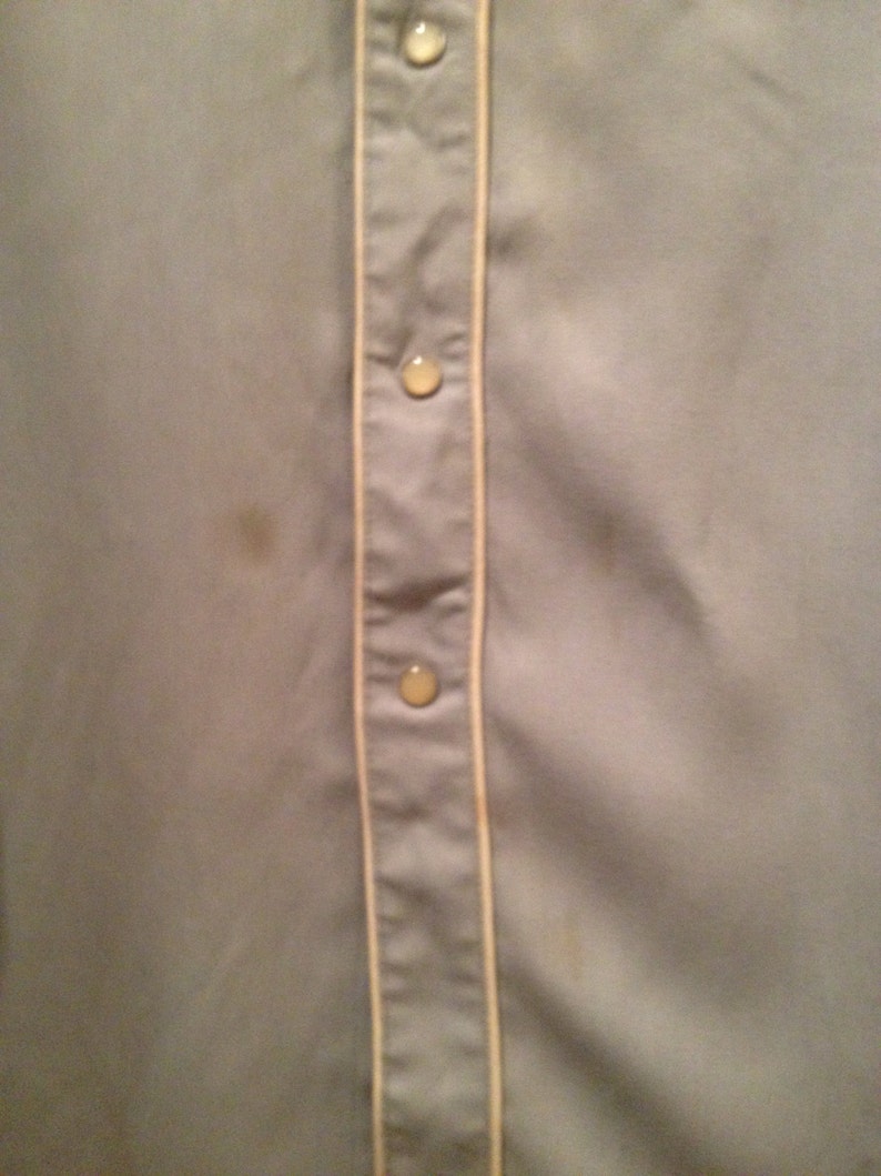 May include: A light gray button-up shirt with a white trim down the front. The shirt has three buttons visible.