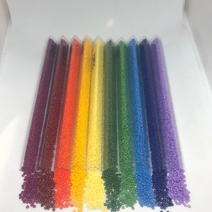 May include: Assortment of colorful seed beads in clear plastic tubes. The beads are arranged in a rainbow pattern, with red, orange, yellow, green, blue, and purple beads.