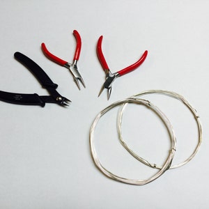 Può includere: Due paia di pinze con manico rosso e un paio di pinze tagliafili nere, insieme a due bobine di filo d'argento.