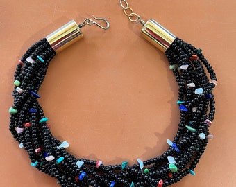 May include: A multi-strand necklace with black beads and colorful gemstone accents. The necklace has a gold clasp and is approximately 18 inches long.