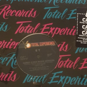 May include: A black vinyl record with a white label. The label has the text "Total Experience" in a circle with a butterfly logo. The text "ET" is printed below the logo. The record title is "Candy (Long Radio Version)".