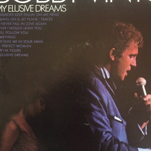 May include: A black and white vinyl record album cover featuring a photo of Bobby Vinton singing into a microphone. The album title is "My Elusive Dreams" and the text "Drops Keep Fallin' On My Head" is also visible.