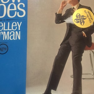 May include: A man in a black suit and black shoes is sitting on a stool. He is smiling and looking up. He is wearing a yellow button with a blue ribbon and the text "Give the gift of music."