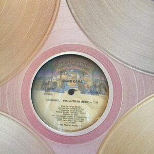 May include: A white vinyl record with a pink label. The label features the text "Casablanca Records and Films" in a black and gold font. The record is titled "Flashdance... What a Feeling (Remix)" by Irene Cara. The record is 45 RPM and stereo.