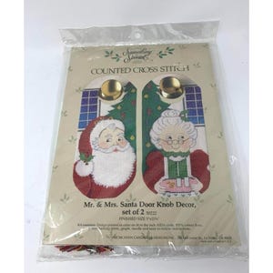 May include: A counted cross stitch kit featuring Mr. & Mrs. Santa Door Knob Decor. The kit includes a design printed in color on 14 count Aida cloth, backing fabric, graph, needle and easy-to-follow instructions. Finished size is 5 x 11 inches.  The kit is from Candamar Designs Inc.