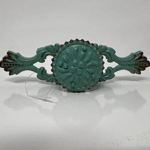 May include: A teal blue metal drawer pull with a decorative floral design. The pull has a rustic finish and is perfect for adding a touch of farmhouse style to your home.
