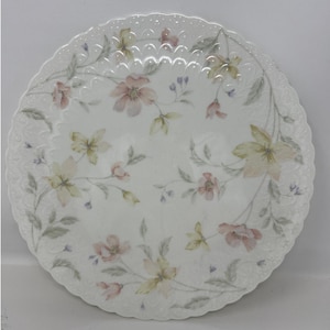 Könnte beinhalten: Ein weißer Keramik-Dinnerteller mit einem gewellten Rand und einem Blumendesign. Die Blumen sind rosa, gelb und grün.