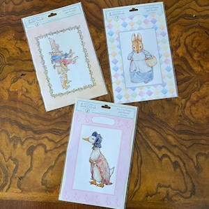 May include: Three packages of Peter Rabbit Beatrix Potter die-cut frames and accents. One features a group of rabbits in a floral border, one shows a rabbit with a basket on a diamond background, and one depicts a duck in a bonnet and shawl.