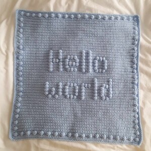 May include: A light blue crocheted baby blanket with a raised "hello world" design.
