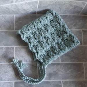 May include: A light blue crocheted baby bonnet with a long tie. The bonnet has a textured, raised pattern.