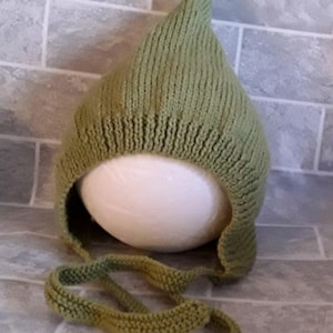 May include: A green knitted baby hat with a pointed top and a long tie. The hat is made of a soft, warm yarn and is perfect for keeping a baby's head warm in the winter.