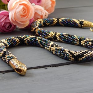 May include: A beaded snake necklace with a gold-toned snake head charm. The necklace is made with black, gold, and iridescent beads.